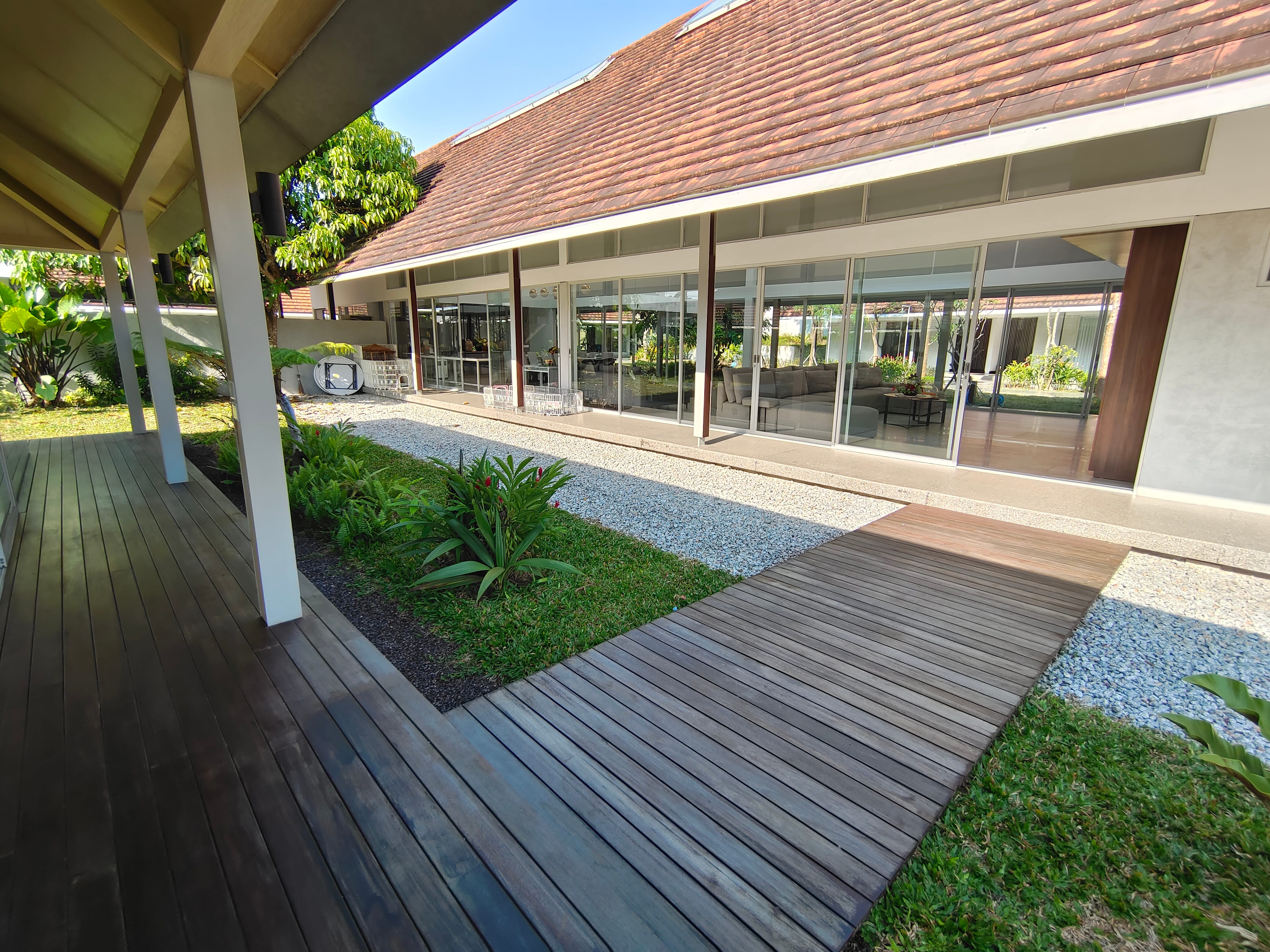 Wide view of hardwood decking along exterior of Kowi Bangka residence with garden by Reywood Indonesia
